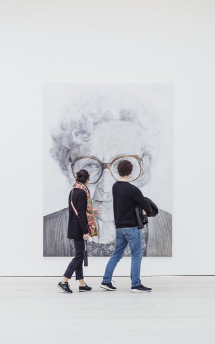 Grande retrato de idosa em preto e branco com duas pessoas olhando para o quadro